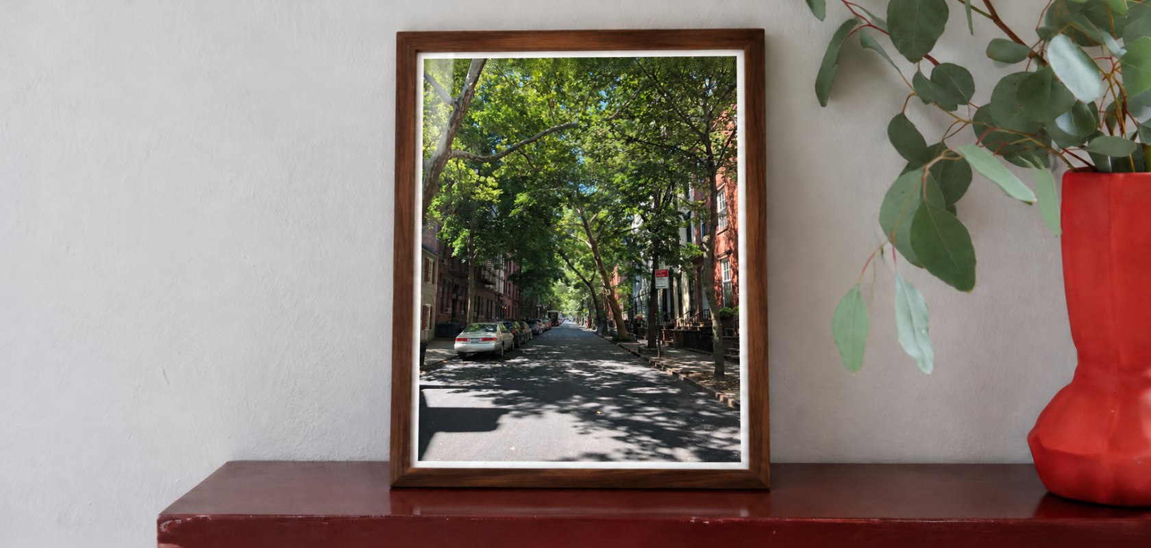 Una fotografía de una calle arbolada de 15 por 21 en un marco de madera sobre una pared clara.